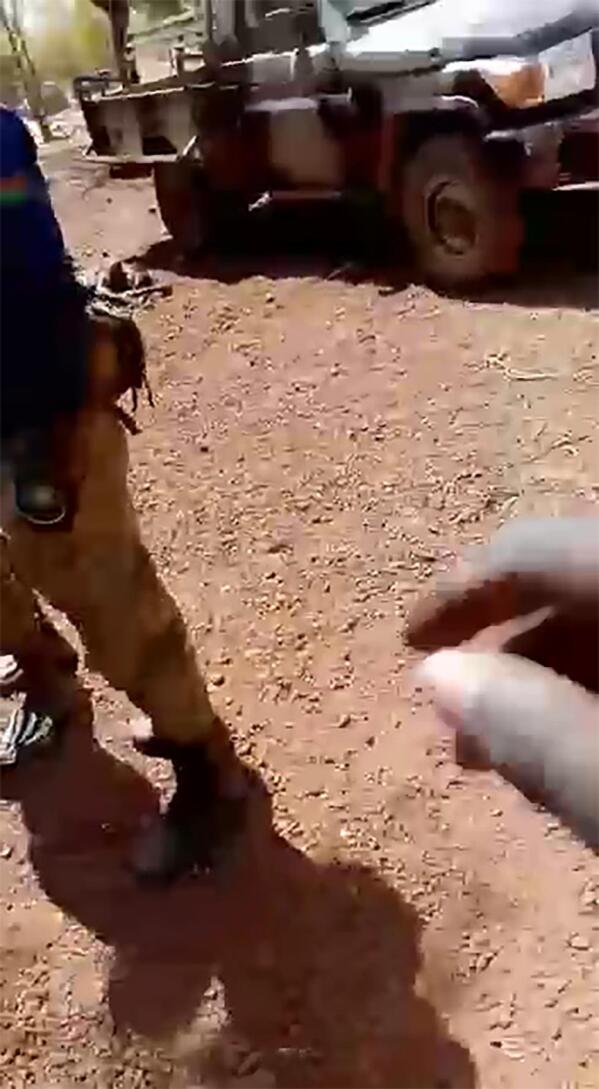 A soldier with the Burkina Faso flag on the shoulder of his shirt stands near the body of a dead child in a frame grab from a video that began circulating on social in the country in mid-February. The 83-second includes video shows the bodies of seven boys, including one whose head is seen being smashed in with a large rock. (WhatsApp via AP)