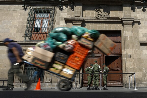 FILE - A man pulls a cart full of merchandise past the National Palace in Mexico City, Dec. 5, 2019. Protesters commandeered a pickup truck Wednesday, March 6, 2024, and used it to ram down the wooden doors of the National Palace where the president lives and hold his daily press briefings, before they were driven off by security agents. (AP Photo/Rebecca Blackwell, File)