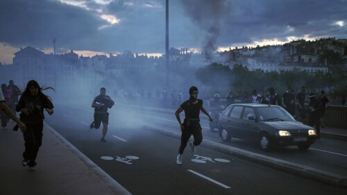 La gente huye durante los enfrentamientos con la policía en el centro de Lyon, centro de Francia, el viernes 30 de junio de 2023. El presidente francés, Emmanuel Macron, instó el viernes a los padres a mantener a los adolescentes en casa y propuso restricciones en las redes sociales para sofocar los disturbios que se extienden por Francia por la muerte tiroteo policial de un conductor de 17 años.  En la pared se lee en francés "Justicia para Nahel" (AP Photo/Laurent Cipriani)