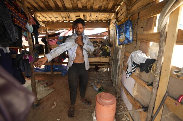 Aamir Shekh puts on a shirt before heading out in a heat wave to a garbage dump on the outskirts of Jammu, India, Wednesday, June 19, 2024. Shekh and his family are among millions of people who scratch out a living searching through India's waste — and climate change is making a hazardous job more dangerous than ever. (AP Photo/Channi Anand)