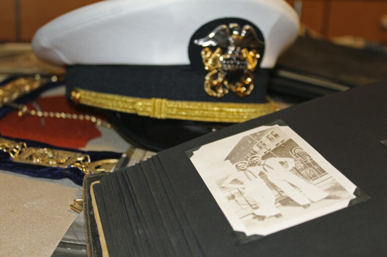 A white US Navy cap, Navy memorabilia and old photographs displayed on Pearl Harbor survivor Ira's kitchen table "ike" Schaub, 103, at his home in Beaverton, Ore., on Monday, Nov. 20, 2023.  Scheib was in the Navy and on the USS Dobbin during the Pearl Harbor attacks on December 7, 1941.  Eighty-two years later, Sheb plans to return to Pearl Harbor on the anniversary of the attack to remember the more than 2,300 soldiers who died.  (AP Photo/Claire Rush)