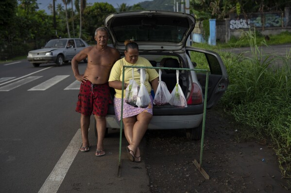A couple sells bags of freshly caught tuna by the side of the road in Teahupo'o, Tahiti, French Polynesia, Tuesday, Jan. 16, 2024. (AP Photo/Daniel Cole)