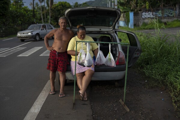 A couple sells bags of freshly caught tuna on the side of the road in Te Aupoo, Tahiti, French Polynesia, on Tuesday, January 16, 2024.  (AP Photo/Daniel Cole)