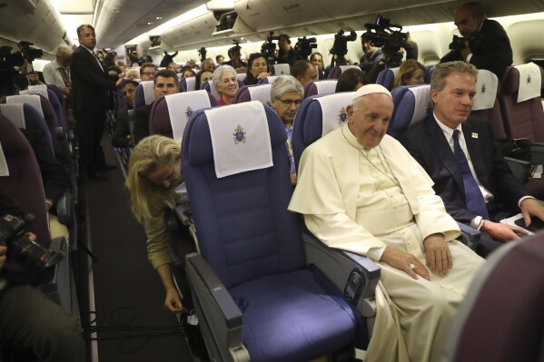 Pope Francis sits next to Greg Burke, right, with journalists after turbulence interrupted his news conference, during a flight from Lima, Peru, to Rome, Jan. 21, 2018. (AP Photo/Alessandra Tarantino)