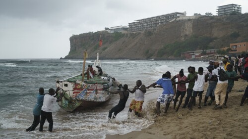 Las personas trabajan juntas para sacar un bote volcado a tierra donde varias personas fueron encontradas muertas en Dakar, Senegal, el lunes 24 de julio de 2023, según residentes locales.  Los cuerpos fueron descubiertos por marineros temprano en la mañana y se cree que son inmigrantes debido al tipo de bote en el que viajaban.  (Foto AP/Leo Correa)