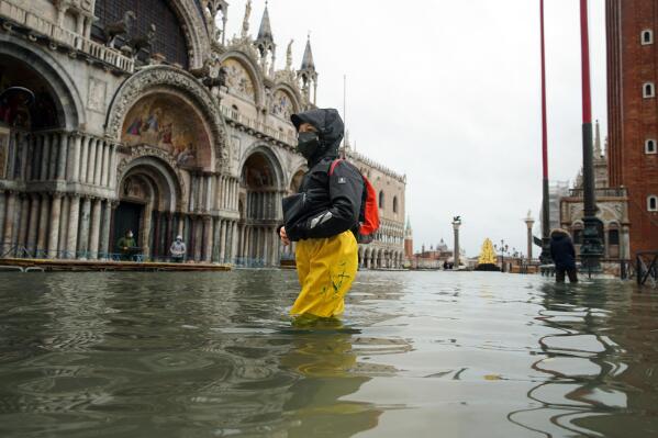 FILE - In this Tuesday, Dec. 8, 2020 file photo, people wade their way through water in flooded St. Mark's Square following a high tide, in Venice, Italy.  Lashing winds that pushed 1.87 meters (nearly 6 feet 2 inches) of water into Venice in November 2019 and ripped the lead tiles off St. Mark’s Basilica for the first time ever shocked Venetians with the city’s second-worst flood in history, but it was the additional four exceptional floods over the next six weeks that triggered fears about the impact of worsening climate change.  (Anteo Marinoni/LaPresse via AP, file)