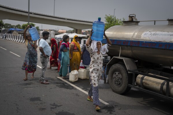 FILE - Rekha Devi, a 30-year-old farm worker, carries drinking water from a municipality water tanker to her temporary shelter on an under construction overpass after her family evacuated the flooded banks of the Yamuna River in New Delhi, India, Wednesday, Aug. 9, 2023. Devi, her husband and their children fled as July's record monsoon rains triggered flooding that killed more than 100 people in northern India, displaced thousands and inundated large parts of the capital city. (AP Photo/Altaf Qadri, File)