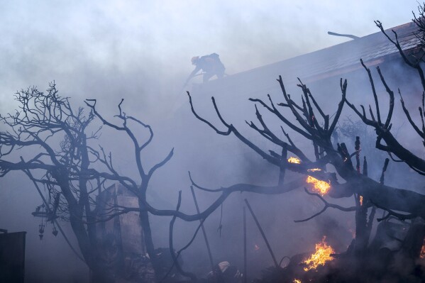 A firefighter tries to contain the Palisades Fire from a rooftop in the Pacific Palisades neighborhood of Los Angeles, Tuesday, Jan. 7, 2025. (AP Photo/Ethan Swope)