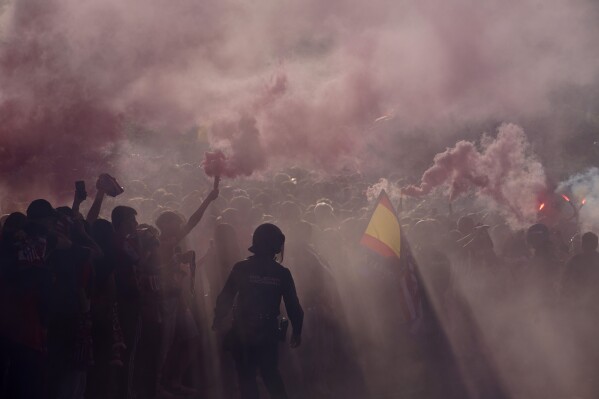Police officers stand guard as supporters burn flares outside the Metropolitano stadium, ahead of the Champions League quarterfinal first leg soccer match between Atletico de Madrid and Dortmund in Madrid, Spain, Wednesday, April 10, 2024. (AP Photo/Andrea Comas)