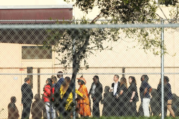 Nine members of Congress wait to enter Marjory Stoneman Douglas High School, Friday, Aug. 4, 2023, in Parkland, Fla. The group will tour the blood-stained and bullet-pocked halls, shortly before ballistics technicians reenact the massacre that left 14 students and three staff members dead in 2018. The reenactment is part of a lawsuit filed by the victims' families against former Deputy Scot Peterson and the Broward Sheriff's Office. (AP Photo/Marta Lavandier)