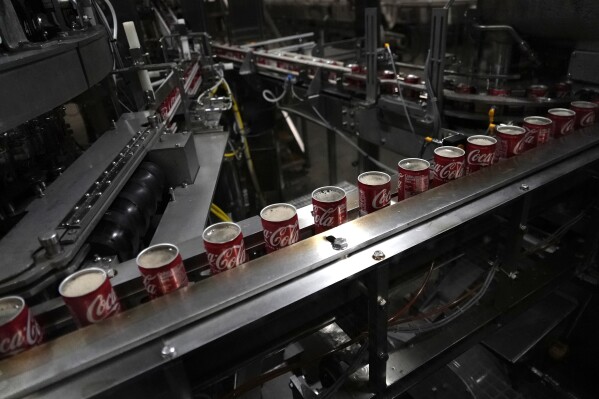 Coca-Cola cans move down a conveyer belt in the Swire Coca-Cola bottling plant Oct. 20, 2023, in Denver. Major corporations in water-guzzling industries such as apparel, food and beverage, and tech want to be better stewards of the freshwater resources they use. Coca-Cola said its water use in 2022 was about 10% more efficient compared to 2015. (AP Photo/Brittany Peterson)