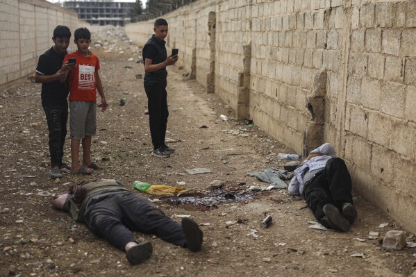 LƯU Ý CỦA EDS: NỘI DUNG ĐỒ HỌA - Những cậu bé Syria dùng điện thoại di động chụp ảnh thi thể của cựu thị trưởng thị trấn Shanaya là Houssam Warawar và con trai ông là Haidar, những người đã thiệt mạng tại thị trấn Sahnaya, phía nam Damascus, Syria, thứ năm, ngày 1 tháng 5 năm 2025, một ngày sau khi các cuộc đụng độ nổ ra giữa các thành viên của giáo phái thiểu số Druze và các chiến binh ủng hộ chính phủ. (Ảnh AP/Ghaith Alsayed)