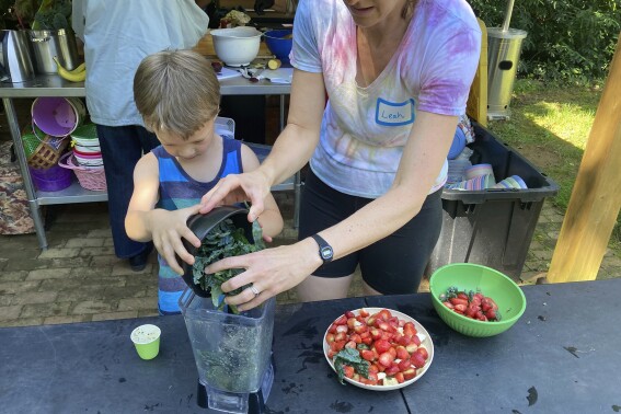 2024年5月29日，星期三，北卡罗来纳州希尔斯堡的春天森林，“成长之旅”组织者Leah Reichardt-Osterkatz（右）正在帮助孩子们用他们摘下的草莓和农场种植的甘蓝制作冰沙。（Yonat Shimron/宗教新闻社通过美联社）
