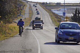 A biker leads a line of cars driving off the Homer Spit at about on Monday, Oct. 19, 2020, in Homer, Alaska after a tsunami evacuation order was issued for low-lying areas in Homer. (Michael Armstrong/Homer News via AP)