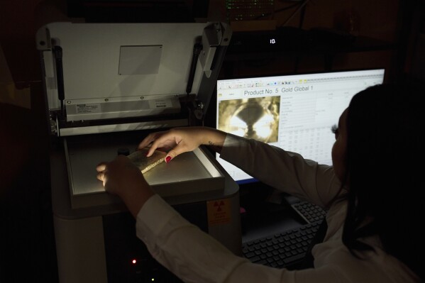 Sarahi Cervantes places a gold bar on an X-ray machine for assaying at A&M Precious Metals in the St. Vincent Jewelry Center in the Jewelry District of Los Angeles, Friday, May 2, 2025. (AP Photo/Jae C. Hong)