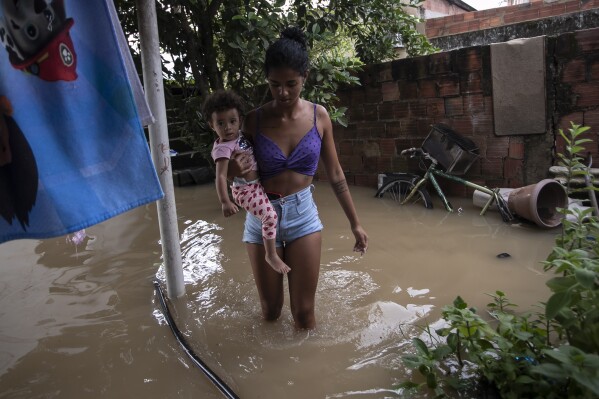 Ingrid Monteiro carries her one-year-old daughter Aylla Perola over floodwaters outside their home after deadly, heavy rainfall in Duque de Caxias, Brazil, Sunday, Jan. 14, 2024. (AP Photo/Bruna Prado)