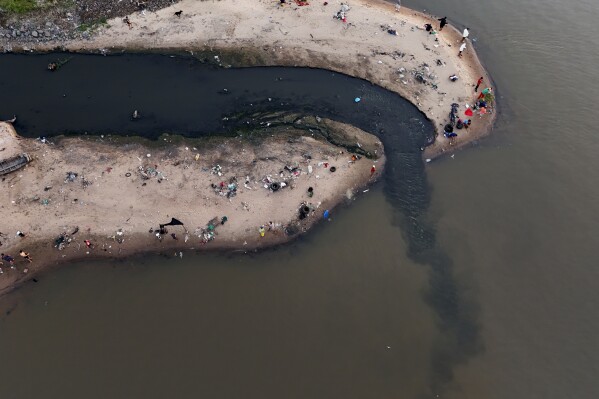 La gente pesca cerca del drenaje que desemboca en el río Paraguay, en Asunción, Paraguay, el domingo 28 de enero de 2024. (Foto AP/Jorge Saenz)