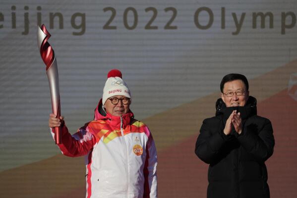First Torch bearer Luo Zhihuan holds up the torch after receiving it from Chinese Vice Premier Han Zheng before the start of the torch relay for the 2022 Winter Olympics at the Olympic Forest Park in Beijing on Wednesday, Feb. 2, 2022. (AP Photo/Sam McNeil)