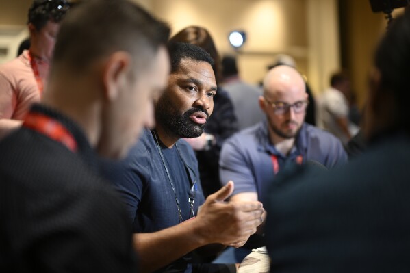 New England Patriots head coach Jerod Mayo, center, talks with reporters during an AFC coaches availability at the NFL owners meetings, Monday, March 25, 2024, in Orlando, Fla. (AP Photo/Phelan M. Ebenhack)