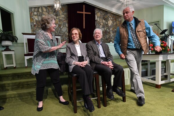 In this Sunday, Nov. 3, 2019, photo, former President Jimmy Carter, second from right, and former first lady Rosalynn Carter sit, as guests Romona Kluth, left, and husband Doug Kluth, from Nebraska, finish their turn of having their photo made with them, after Sunday school at Maranatha Baptist Church, in Plains, Ga. (AP Photo/John Amis)