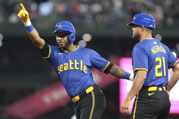 Seattle Mariners' Victor Robles, left, celebrates next to first base coach Kristopher Negrón (21) after getting a hit off Texas Rangers pitcher Andrew Heaney during the first inning of a baseball game, Friday, June 14, 2024, in Seattle. (AP Photo/Jason Redmond)