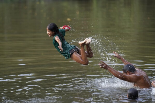 Indigenous leader and councilman Francisco Oro Waram plays with a girl in the Komi Memem River, named Laje in non-Indigenous maps, at his Wari' community in Guajara-Mirim, Rondonia state, Brazil, Friday, July 14, 2023.  (AP Photo/Andre Penner)