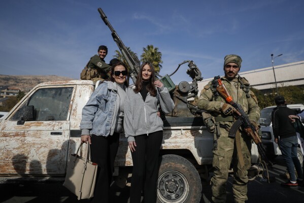 Women pose for a photograph with opposition fighters in Damascus, Syria, Tuesday, Dec. 10, 2024. (AP Photo/Omar Sanadiki, File)