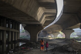 Meera Devi, left, accompanies her daughter Arima, 7, to her school as they walk on the flood plain of Yamuna River, in New Delhi, India, Friday, Sept. 29, 2023. Their family was among those displaced by the recent floods in the Indian capital's Yamuna River. Storms, floods, fires and other extreme weather events led to more than 43 million displacements involving children between 2016 and 2021, according to a United Nations report. (AP Photo/Altaf Qadri)