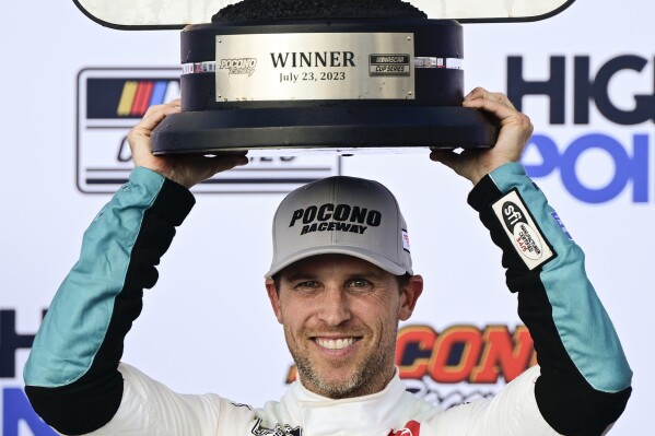 Denny Hamlin poses with the trophy in Victory Lane after winning a NASCAR Cup Series auto race at Pocono Raceway, Sunday, July 23, 2023, in Long Pond, Pa. (AP Photo/Derik Hamilton)