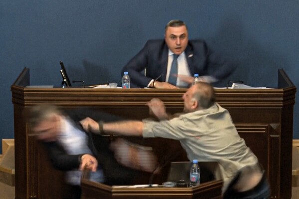 This photo taken from video released by Georgian Parliament on Monday, April 15, 2024, shows the leader of the ruling Georgian Dream party's group in parliament, Mamuka Mdinaradze, left, being punched in the face by opposition MP Alexander Elisashvili while speaking in Tbilisi, Georgia. That then sparked a wider fight between several other lawmakers. Georgian Dream, the governing party in the country of Georgia, said earlier this month that it would resubmit a draft law calling for media and non-commercial organizations to register as being under foreign influence if they receive more than 20% of their budget from abroad. (Georgian Parliament via AP)