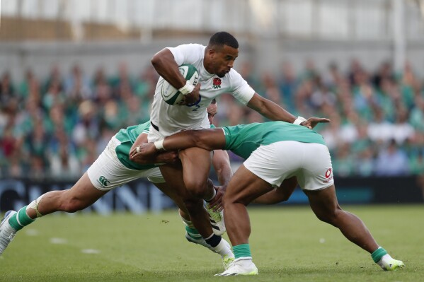 England's Anthony Watson, centre, is challenged by Ireland's players during the international rugby union match between Ireland and England, at Aviva Stadium, Dublin, Ireland, Saturday, Aug. 19, 2023. (AP Photo/Peter Morrison)
