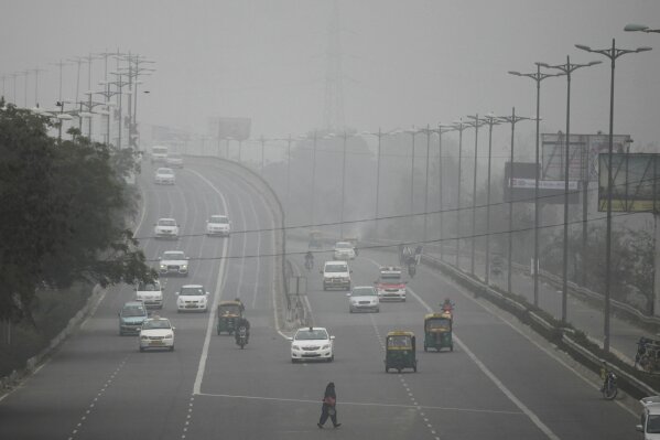 FILE - In this Jan. 15, 2016, file photo, an Indian woman crosses a road as vehicles move through morning smog on the last day of a two-week experiment where the Delhi government allowed private cars on the roads on alternate days depending on whether their license plates end in an even or an odd number, to reduce the number of cars to fight pollution in New Delhi, India. Indian authorities announced an odd-even scheme for movement of private cars in the Indian capital from Nov. 4-15, 2019, after a major Hindu festival that features massive fireworks cloaking the area with toxic smog and dust. (AP Photo/Altaf Qadri, File)