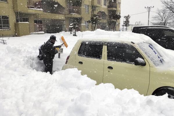 A resident shovels snow off around a car at a parking lot in Kitami city Hokkaido prefecture, northern Japan, on Dec. 24 2022. (Kyodo News via AP)