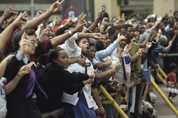 FILE — A crowd of people sing and give peace signs during a lunchtime peace march in downtown Johannesburg, South Africa, Jan. 27, 1994 ahead of the country's all race elections. (AP Photo/Denis Farrell/File)