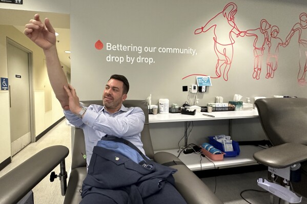 Aaron Posey, a Bloodworks Northwest executive, puts pressure where the needle entered his arm after donating blood at the blood center's Seattle headquarters on Dec. 14, 2023. New federal guidelines that dropped an abstinence requirement before gay men in monogamous relationships can give blood are opening a new pool of potential donors. Posey, whose own life was saved by a transfusion when he fell down a set of stairs and broken glass sliced an artery, welcomed the new guidance, saying hospitals and patients need access to a new pool of donors. (AP Photo/Manuel Valdes)