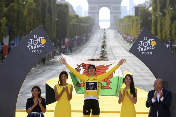 Tour de France winner Britain's Geraint Thomas, wearing the overall leader's yellow jersey, and draped in the flag of Wales celebrates on the podium after the twenty-first stage of the Tour de France cycling race over 116 kilometers (72.1 miles) with start in Houilles and finish on Champs-Elysees avenue in Paris, France, Sunday July 29, 2018. (Stephane Mantey, pool via AP, File)