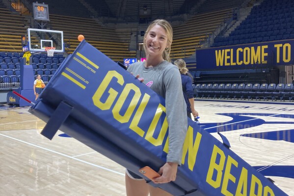 California assistant volleyball coach Savannah Rennie carries equipment in Berkeley, Calif., Nov. 2, 2023. Rennie knows how remarkable her volleyball path has been to bring her back to where it all started. At age 18 and a freshman at Cal, she was diagnosed with a life-threatening liver condition and waited nearly 2 ½ months for a transplant at Indiana University that saved her life. Then, she was diagnosed with post-transplant lymphoma and underwent cancer treatment. (AP Photo/Janie McCauley)