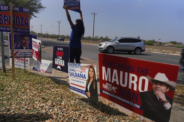 A supporter carries a campaign sign as she greets voters entering the parking lot at a polling place at Lark Community Center on Tuesday, March 5, 2024, in McAllen, Texas. (Joel Martinez/The Monitor via AP)