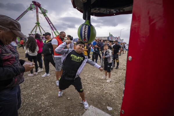 A boy punches a boxing arcade machine at a fair in Hagioaica, Romania, Saturday, Sept. 16, 2023. For many families in poorer areas of the country, Romania's autumn fairs, like the Titu Fair, are one of the very few still affordable entertainment events of the year. (AP Photo/Andreea Alexandru)