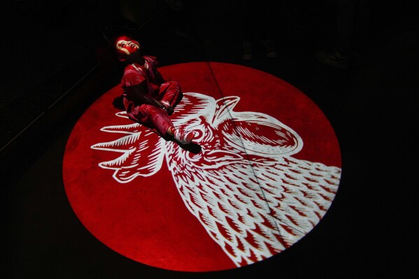 A girl plays under a light projecting a rooster on the floor during nighttime activities in the Chacao neighborhood of Caracas, Venezuela, Saturday, Sept. 2, 2023. (AP Photo/Matias Delacroix)