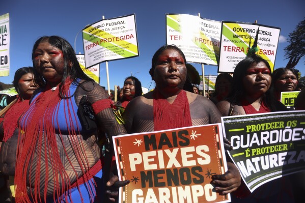 FILE - An Indigenous woman marches with a sign that reads in Portuguese "More fish, less mining," during the 20th annual Free Land Indigenous Camp in Brasilia, Brazil, April 23, 2024. Thousands of Indigenous people continue to march on Thursday, April 25, calling on the government to officially recognize lands they have lived on for centuries and to protect territories from criminal activities like illegal mining. (AP Photo/Luis Nova, File)