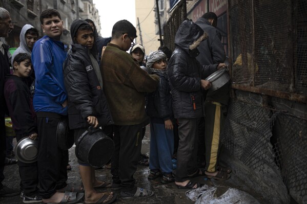 Palestinian children wait in line for food distribution in Rafah, southern Gaza Strip, Wednesday, Dec. 13, 2023. An Israeli military offensive, launched in response to a deadly Oct. 7 Hamas attack, has led to shortages of food, medicine and other basic supplies in Gaza. (AP Photo/Fatima Shbair)