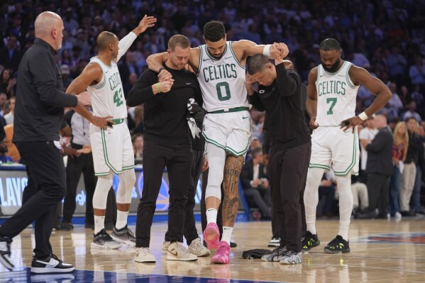 Trainers help Boston Celtics' Jayson Tatum (0) off the court after he was injured during the second half of Game 4 in the Eastern Conference semifinals of the NBA basketball playoffs against the New York Knicks Monday, May 12, 2025, in New York. (AP Photo/Frank Franklin II)