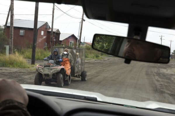 Thomas Noatak, alongside Joseph Moses, carry garbage across Phillips Street during morning pickup, Thursday, Aug. 17, 2023, in Akiachak, Alaska.  (AP Photo/Tom Brenner)