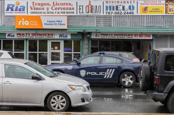 A police car patrols a street in front of a liquor store in Barrio Obrero, San Juan, Puerto Rico, Friday, March 14, 2025. (AP Photo/Alejandro Granadillo)