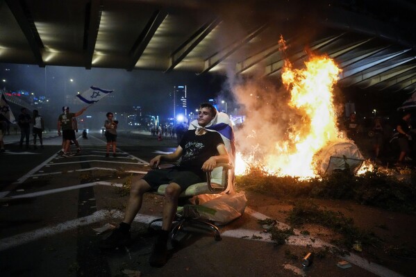 A demonstrator sits next to a bonfire as others occupy the Ayalon Highway to protest against plans by Prime Minister Benjamin Netanyahu's government to overhaul the judicial system in Tel Aviv, Thursday, July 20, 2023. (AP Photo/Ariel Schalit)