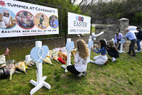 Girls write messages on crosses at an entry to Covenant School, Tuesday, March 28, 2023, in Nashville, Tenn., which has become a memorial for the victims of Monday's school shooting. (AP Photo/John Amis)