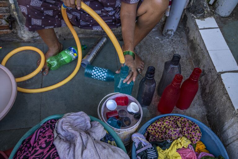 A woman fills bottles with water on her front porch to keep at home in Dharavi, one of Asia's largest slums, in Mumbai, India, Wednesday, May 3, 2023. (AP Photo/Dar Yasin)