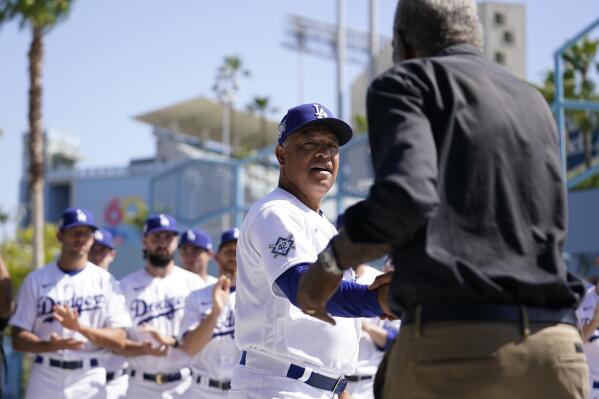 Los Angeles Dodgers' manager Dave Roberts, center, shakes hands with David Robinson, son of Jackie Robinson, before a baseball game between the Cincinnati Reds and the Los Angeles Dodgers in Los Angeles, Friday, April 15, 2022. Today MLB celebrates Jackie Robinson Day, in honor of Robinson, who was the first African American to play in the major leagues. (AP Photo/Ashley Landis)