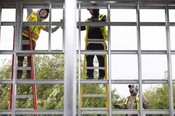 Alaska Native Tribal Health Consortium workers install side paneling for a lift house on Qugtuliaq Road, Thursday, Aug. 17, 2023, in Akiachak, Alaska. (AP Photo/Tom Brenner)